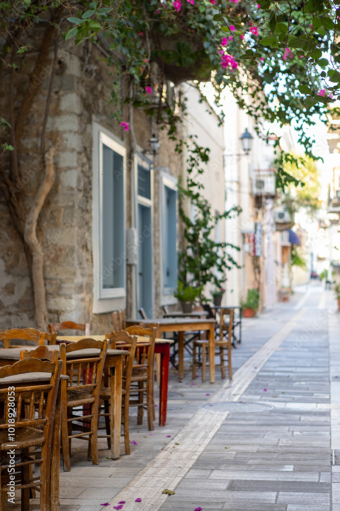 Fototapeta premium In the heart of Nafplio, Greece, rustic wooden tables sit quietly under the shade of lush leaves, creating a perfect setting for relaxed meals and warm conversations.