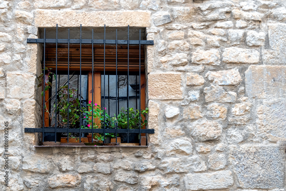 Window of stone built home with iron grates and plants on the sill - common in Spanish pueblos Window of stone built home with iron grates and plants on the sill - common in Spanish pueblos