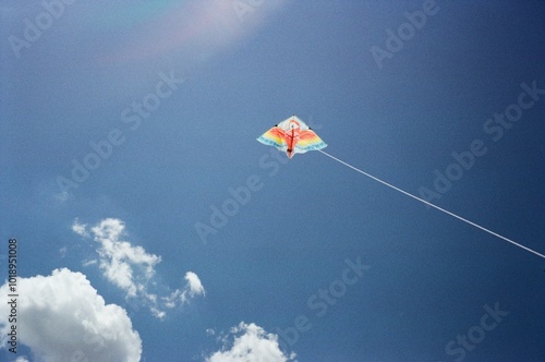 a colorful kite against a blue and white cloudy sky
 photo