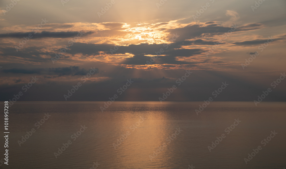 Obraz premium Sun shining through clouds over calm ocean at sunrise