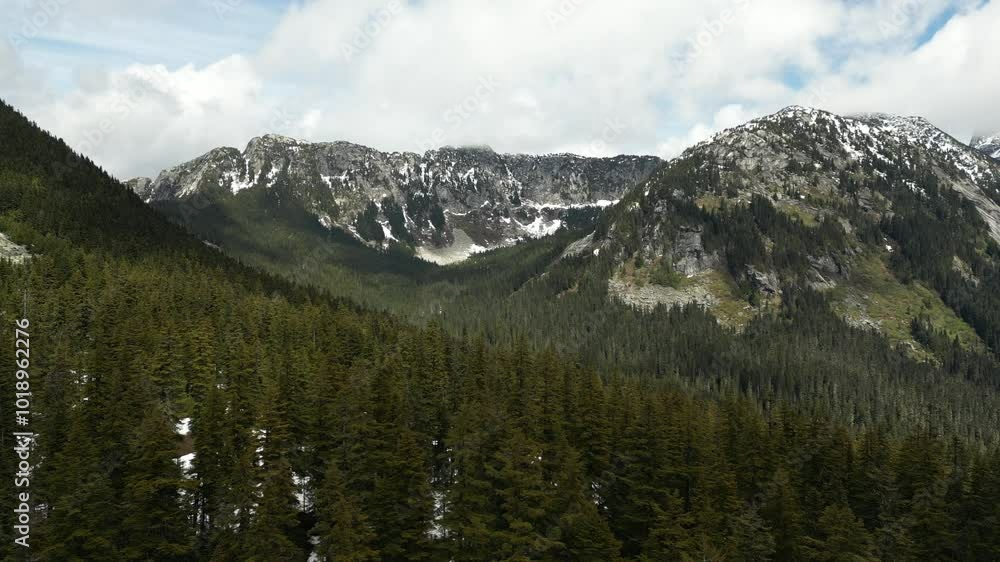 A beautiful mountain landscape with snow capped mountains, a lush green forest, and a blue sky with white clouds. British Columbia, Canada. A beautiful mountain landscape with snow capped mountains, a lush green forest, and a blue sky with white clouds. British Columbia, Canada.