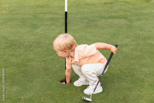 Playful Kid Taking Golf Ball from Flag in Hole photo