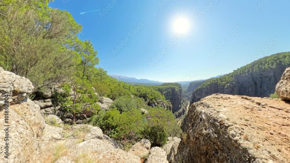 Rocky terrain leads to the edge of a deep Canyon, with the Sun shining brightly in the Sky. The scene captures the rugged Path approaching the Cliff's edge. Zoom in Rocky terrain leads to the edge of a deep Canyon, with the Sun shining brightly in the Sky. The scene captures the rugged Path approaching the Cliff's edge. Zoom in