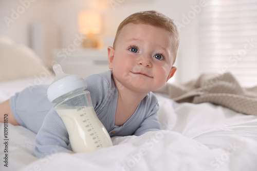 Cute little baby with bottle of milk on bed indoors photo