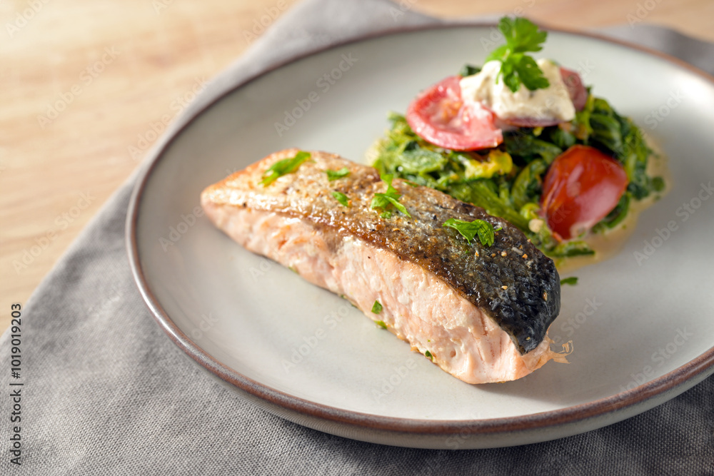 Salmon fillet roasted with a crispy skin, vegetables from cream spinach, onions, tomatoes and parsley garnish, healthy fish meal on a gray plate, low carb diet, copy space Salmon fillet roasted with a crispy skin, vegetables from cream spinach, onions, tomatoes and parsley garnish, healthy fish meal on a gray plate, low carb diet, copy space