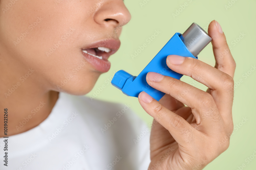 Young woman using asthma inhaler on light green background, closeup Young woman using asthma inhaler on light green background, closeup