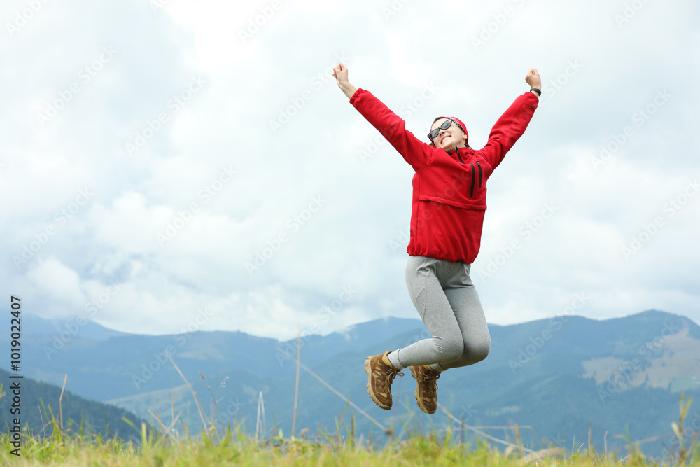 Happy young hiker jumping in mountains, low angle view. Space for text Happy young hiker jumping in mountains, low angle view. Space for text