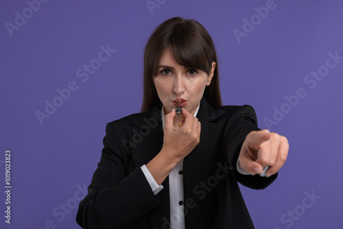 Young woman blowing whistle on purple background