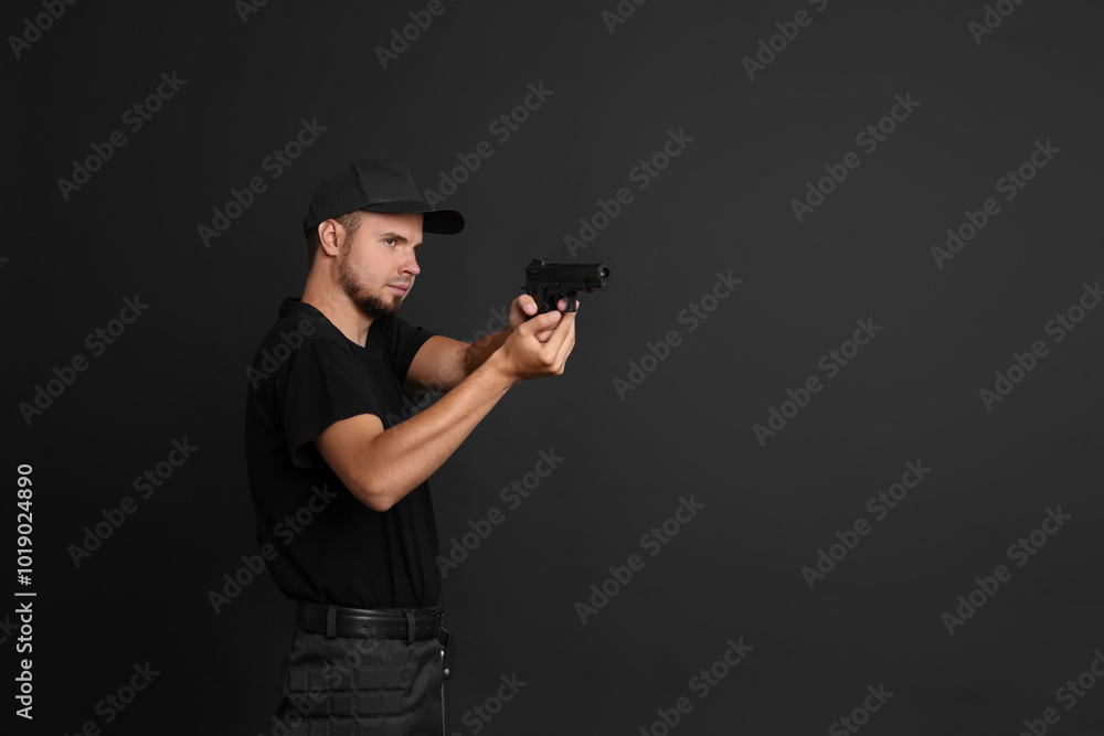 Young bodyguard using gun on black background, space for text Young bodyguard using gun on black background, space for text