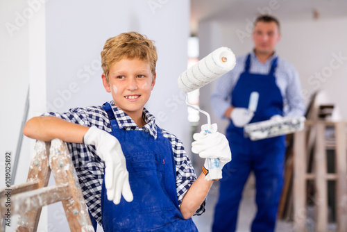 Portrait of emotional boy holding tools for painting wall in house being renovated photo