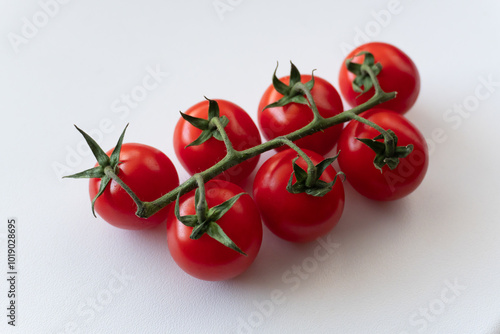 A close-up of a branch with seven cherry tomatoes on a white background. Bright red, ripe cherry tomatoes are captured against a white backdrop. Natural and fresh products. photo