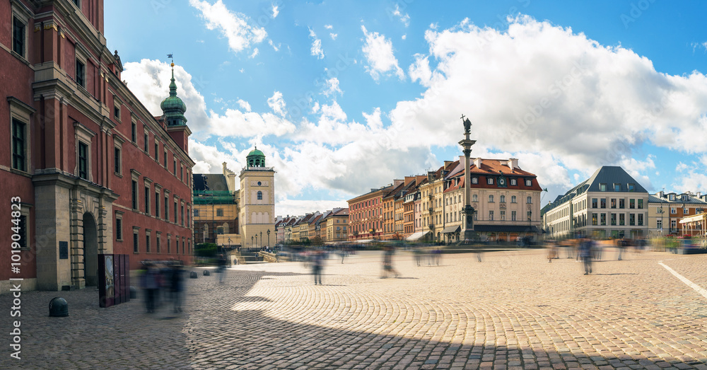 Panoramic view of Warsaw's historic market square under a vibrant blue sky with scattered clouds, showcasing colorful historic buildings and a lively atmosphere. Polish town