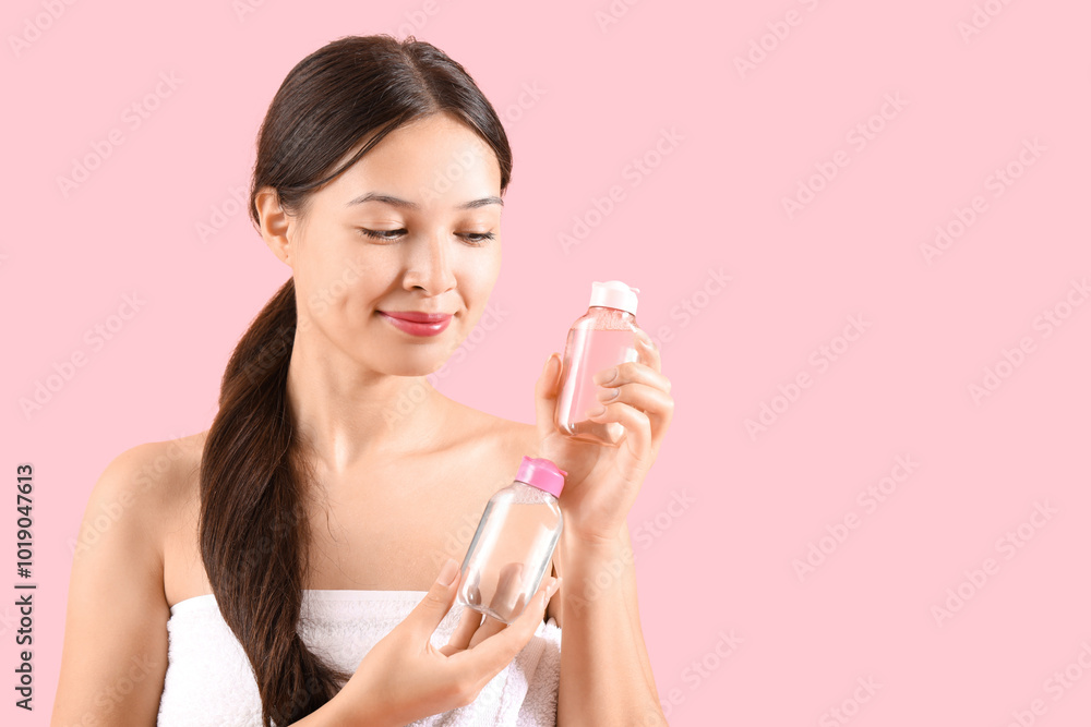 Young Asian woman with bottles of micellar water on pink background, closeup Young Asian woman with bottles of micellar water on pink background, closeup