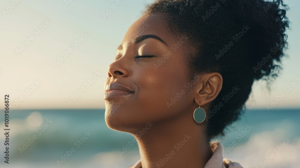 A young woman enjoys a peaceful moment at the beach during sunset while feeling the ocean breeze on her face A young woman enjoys a peaceful moment at the beach during sunset while feeling the ocean breeze on her face