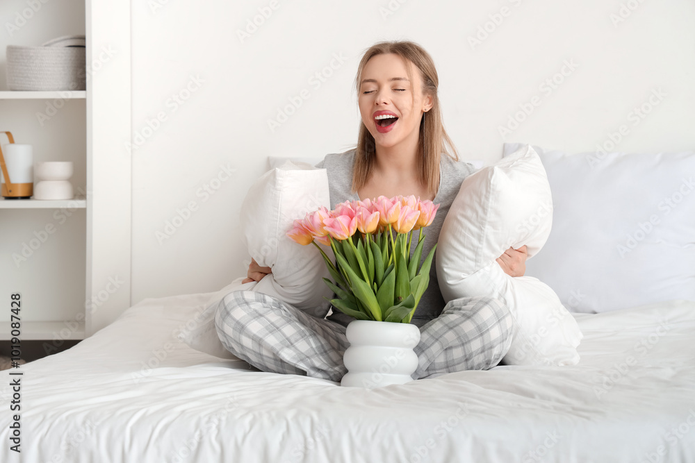 Happy young woman sitting on comfortable bed with bouquet of tulip flowers in bedroom Happy young woman sitting on comfortable bed with bouquet of tulip flowers in bedroom