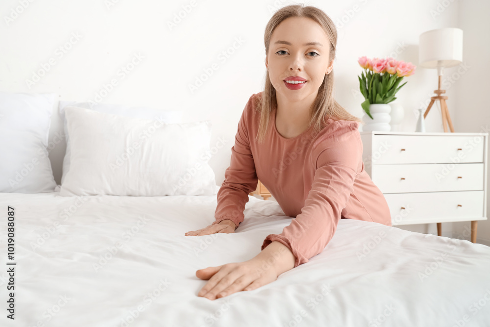 Pretty young woman making bed in light bedroom Pretty young woman making bed in light bedroom
