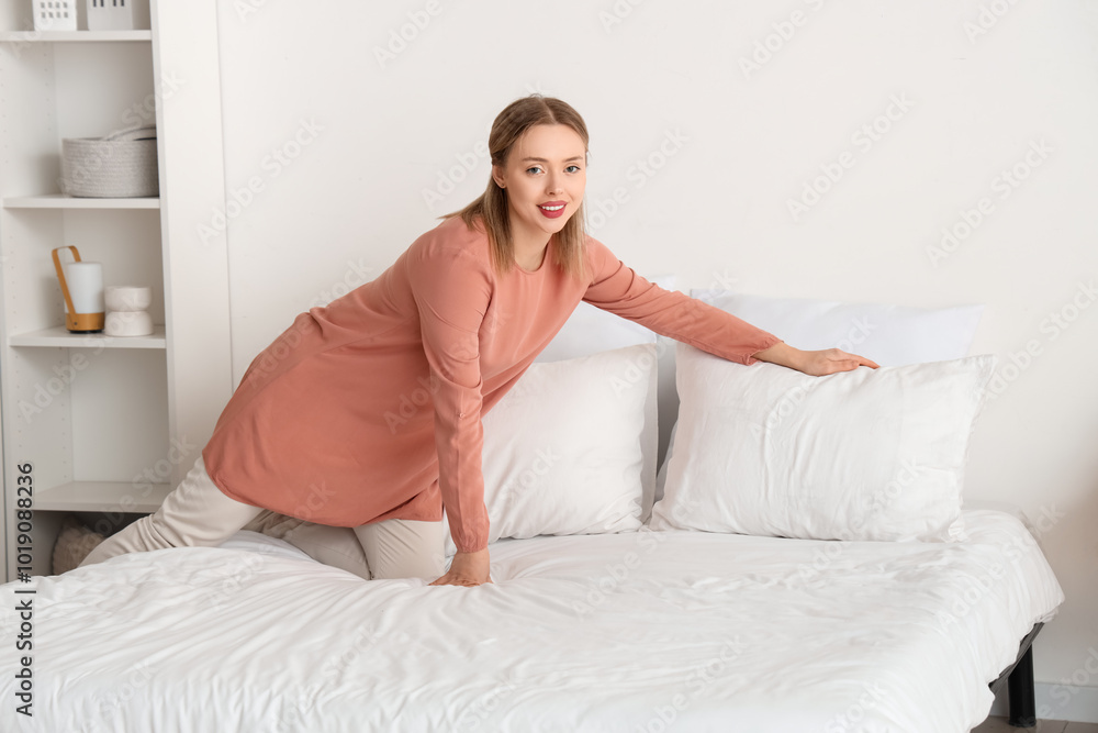 Pretty young woman putting pillow on bed in light bedroom Pretty young woman putting pillow on bed in light bedroom
