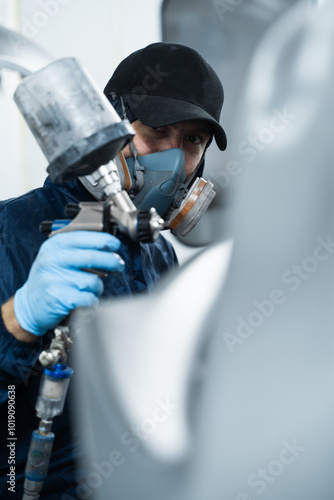 Worker is painting car in dark color with HVLP spray gun. Auto mechanic is changing the color of vehicle using sponge and paint sprayer.