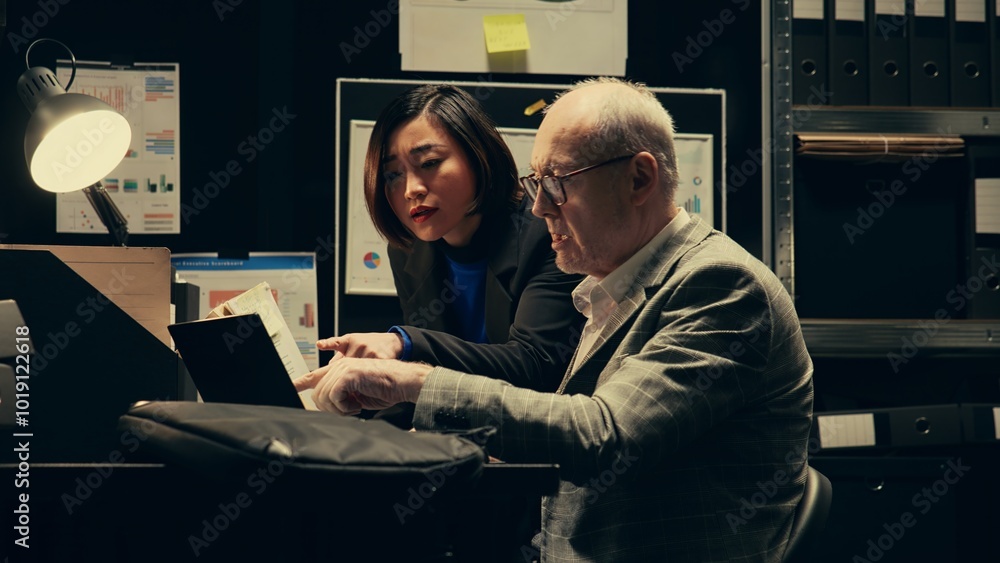 Investigation partners analyze archived autopsy reports and medical records for forensic insights, working in evidence room to gather clues. Law agents team confirm case details. Camera B. Investigation partners analyze archived autopsy reports and medical records for forensic insights, working in evidence room to gather clues. Law agents team confirm case details. Camera B.