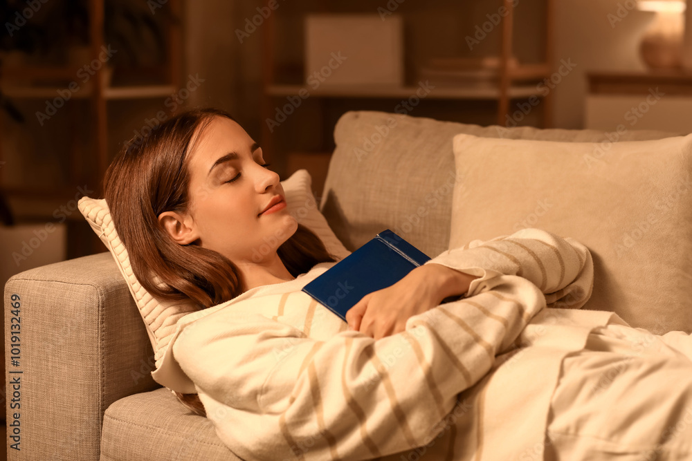 Beautiful young woman with book sleeping on sofa in evening at home Beautiful young woman with book sleeping on sofa in evening at home