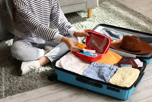 фотографія Young woman with suitcase packing first aid kit at home, closeup