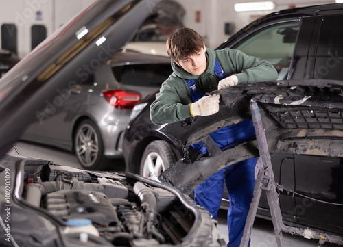 Male mechanic installs new parts instead of old ones on a car in a car service center