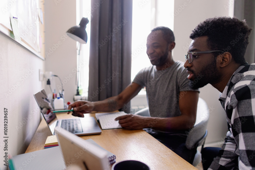Smiling man showing something on laptop to focused young male friend Smiling man showing something on laptop to focused young male friend