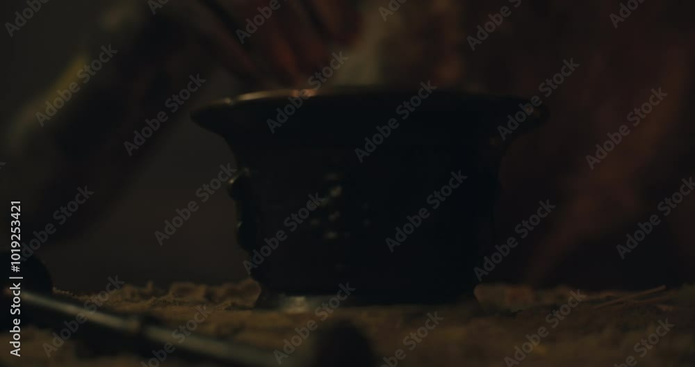 A witch in an old magical hut adds ingredients into the vase with burning embers to cast a curse A witch in an old magical hut adds ingredients into the vase with burning embers to cast a curse