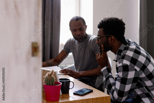 Adult man looking at open copybook while his friend watching at desk