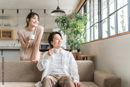 家のリビング・ソファで会話する仲良しの若い日本人夫婦
 photo