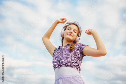 Cute happy smiling girl listening to music and dancing on summer city street