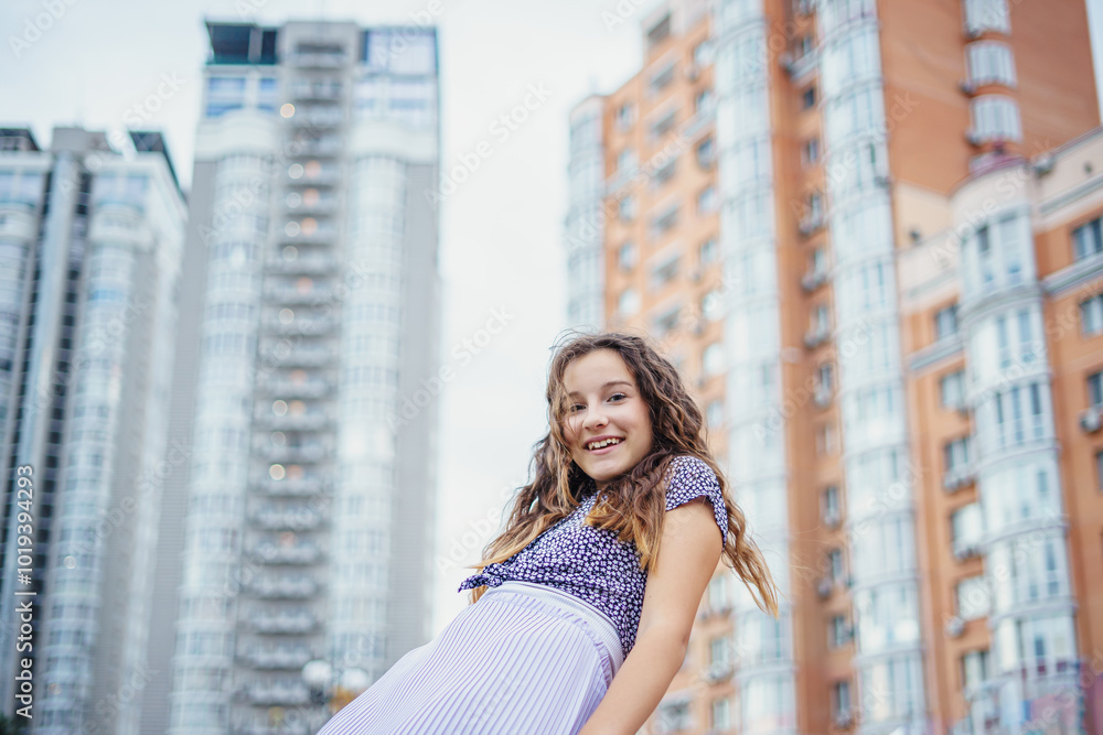 Fototapeta premium Pretty girl in casual clothes against the background of a metropolis street and a skyscraper. View from below