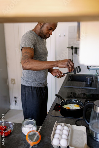 Adult black man with kitchen spatula frying eggs on frying pan photo