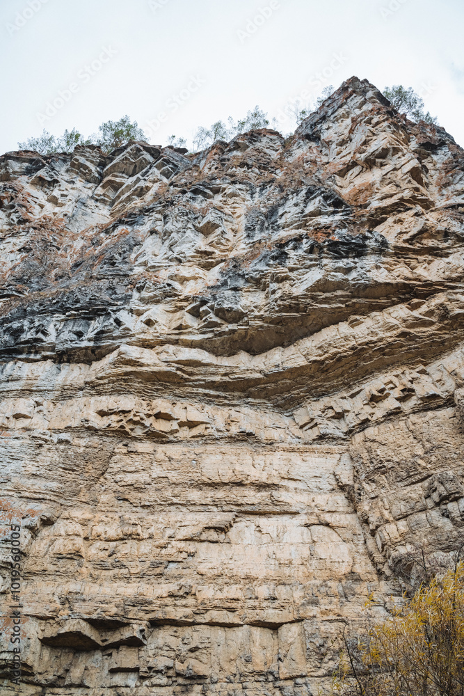 This image showcases a detailed close up of a rugged rocky cliff that towers prominently, with a magnificent mountain visible in the background, enhancing the overall scenic view This image showcases a detailed close up of a rugged rocky cliff that towers prominently, with a magnificent mountain visible in the background, enhancing the overall scenic view