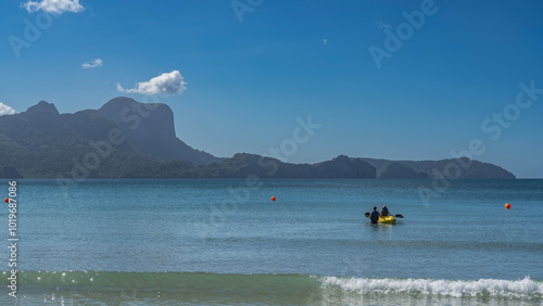 Amazing seascape. Day. The turquoise ocean is calm. The waves are foaming at the shore of the beach. A canoe with people on the water. Picturesque mountains against a clear blue sky. Copy space.  photo