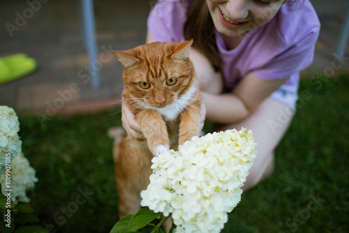 the girl is holding a red cat near a flower photo