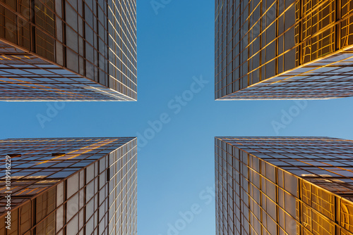 Upward view of modern glass buildings reflecting sunlight against blue photo