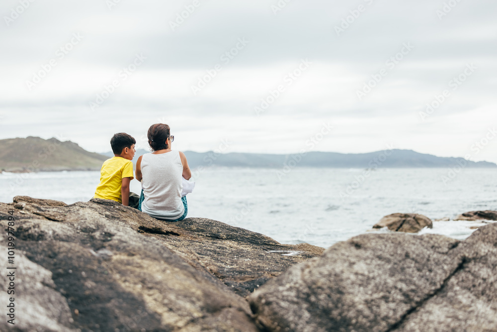 Mother and son enjoying serene ocean view from rocky shore Mother and son enjoying serene ocean view from rocky shore
