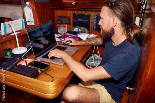 Man works on a laptop in boat's cabin photo