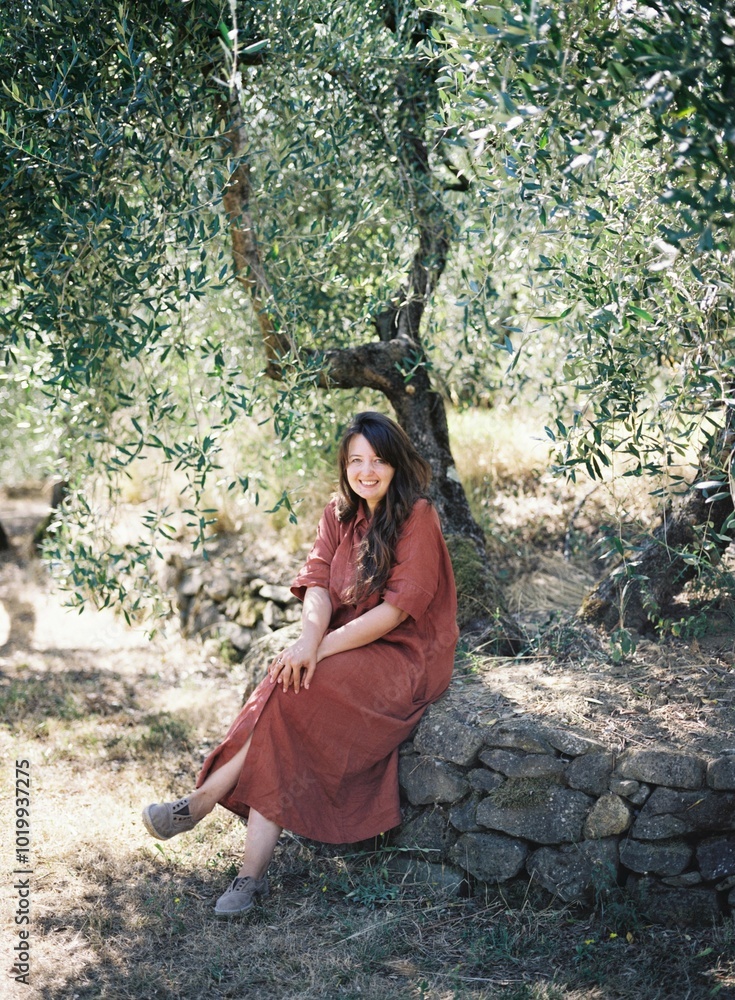Woman in red dress sits under tree with calming smile. Woman in red dress sits under tree with calming smile.