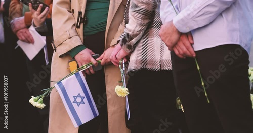 People hold the Israeli flag and flowers during a ceremony commemorating the October 2023 attacks on Israel.
