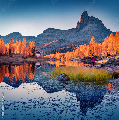 D'Ambrizzola peak reflected in the calm waters of Federa lake. Stunning autumn scene of Dolomite Alps with tourist among orange larch trees on the shore. Colorful morning view of Italy, Europe. photo