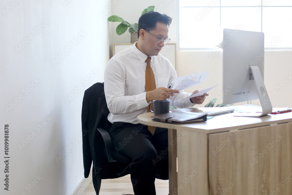 Asian businessman holding and read document paper report while sit at office desk Asian businessman holding and read document paper report while sit at office desk