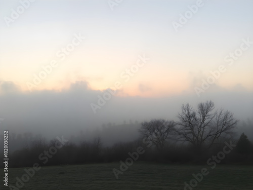 A tranquil scene of a misty sky at dawn, with the landscape partially obscured by fog and the soft light of morning breaking through 