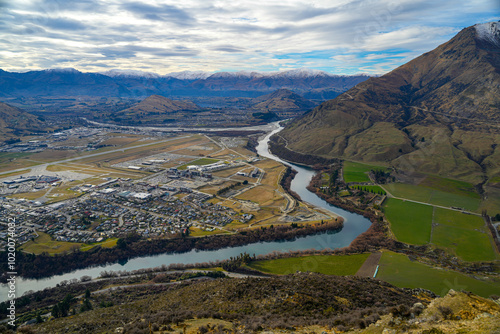 A top-down view of the mountains surrounding Queenstown, with a clear view of the airport nestled in the valley below. A striking combination of nature and man-made structures.
