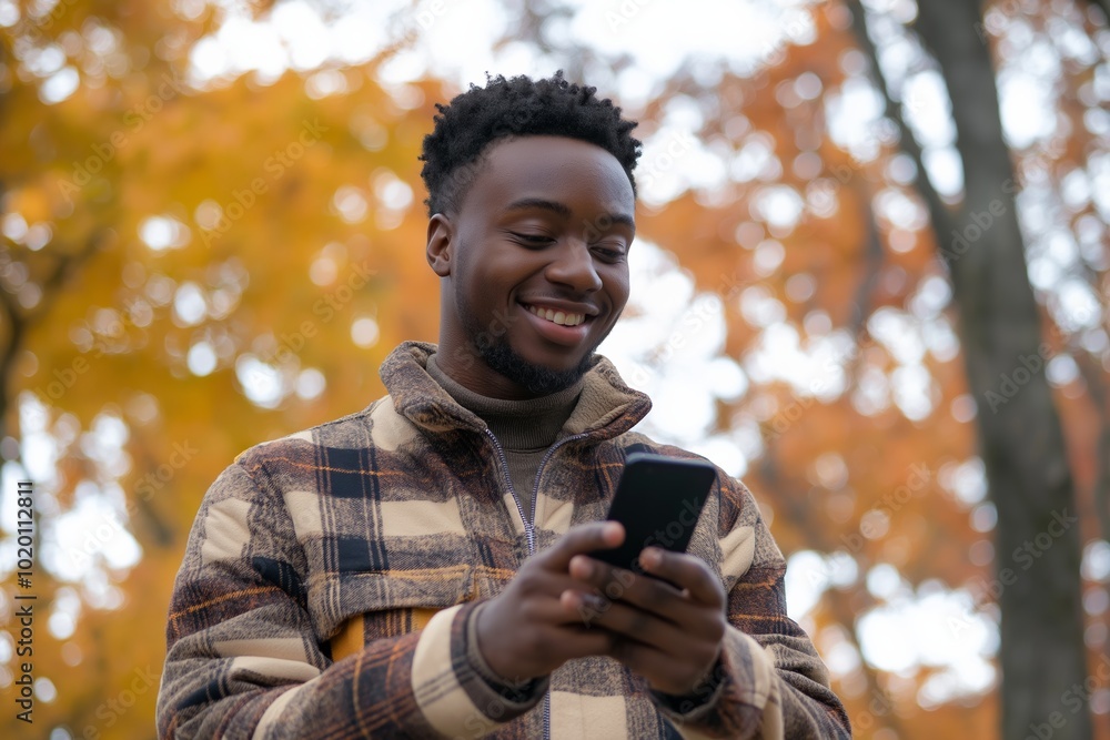 A man with a beard and dreadlocks is smiling while looking at his cell phone. He is wearing a plaid jacket and he is enjoying his time outdoors A man with a beard and dreadlocks is smiling while looking at his cell phone. He is wearing a plaid jacket and he is enjoying his time outdoors
