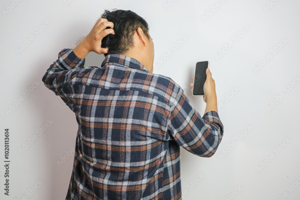 Back view of a man confused looking to the mobile phone that he hold Back view of a man confused looking to the mobile phone that he hold
