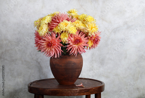 magnificent bouquet of garden dahlias and chrysanthemums in a clay jug on a round table. copy space. garden flowers in a potbellied vase. yellow chrysanthemums and pink dahlias. photo