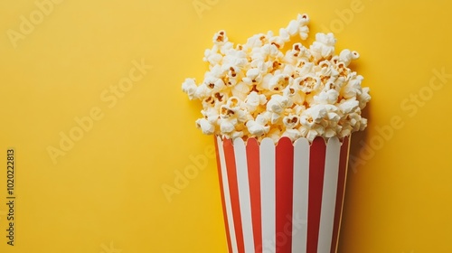 A red and white striped popcorn container overflowing with popcorn on a yellow background.