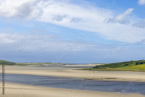 Expansive sandbanks and gentle water channels of the Gweebarra River, Ireland, exposed during low tide beneath a bright sky